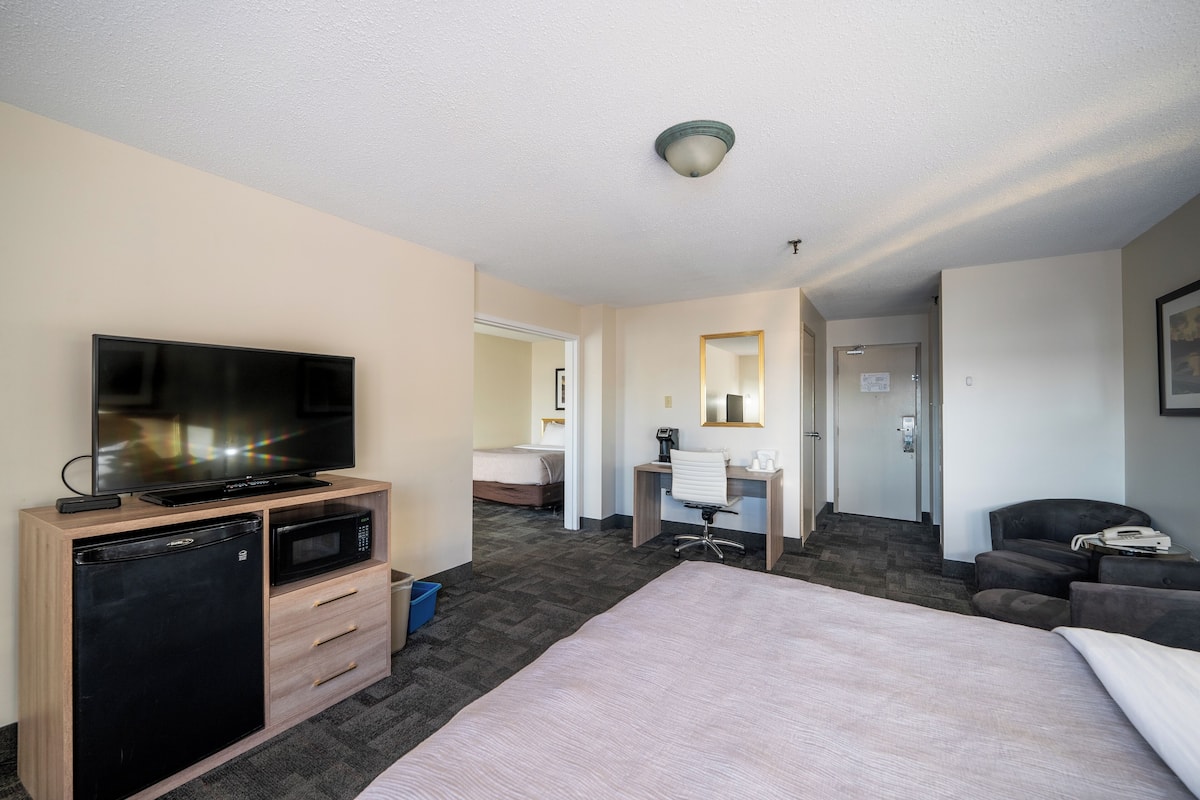 A hotel room with a bed, a TV, a mini-fridge, a desk, and a chair.