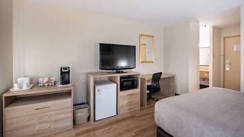 Habitación de hotel con cama, escritorio, computadora, televisión, refrigerador y microondas.