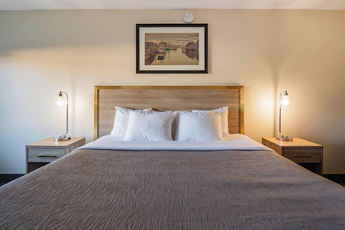 A neatly made bed with a wooden headboard, two bedside lamps, and a framed picture on the wall.