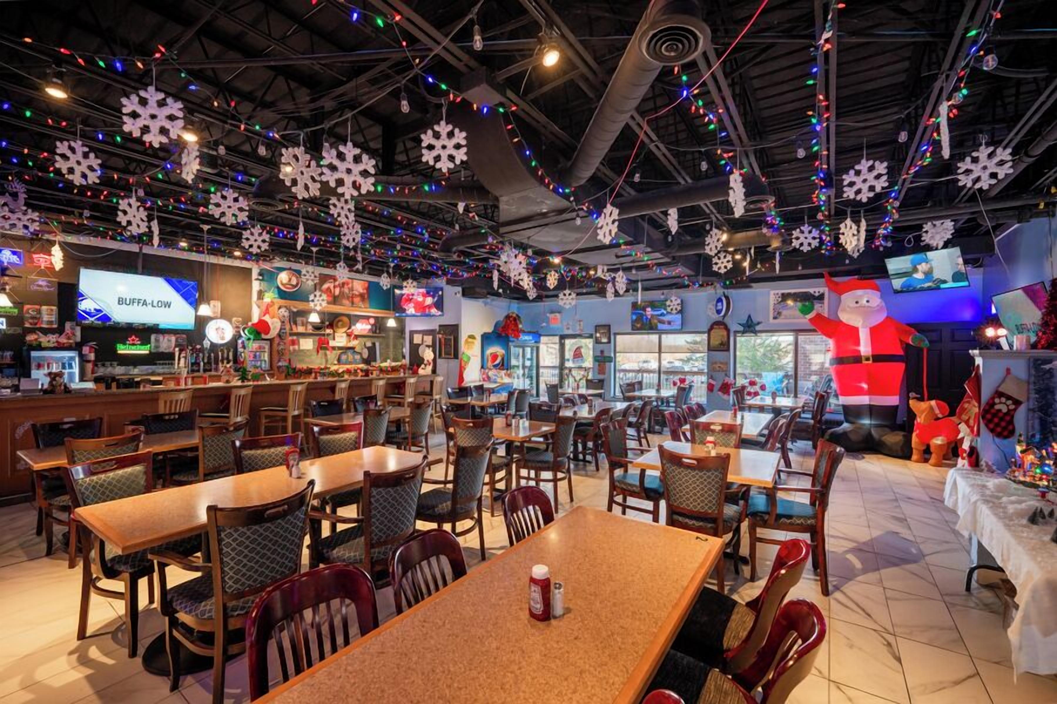 A restaurant with multiple tables and chairs, decorated with snowflakes and Christmas lights.