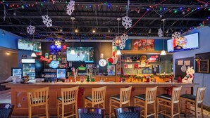 A bar area with wooden chairs and tables, a counter with various items, and festive decorations. - HFX Airport Hotel (Goffs)