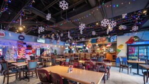 A spacious indoor dining area with multiple tables and chairs, decorated with snowflake ornaments and string lights. - HFX Airport Hotel (Goffs)