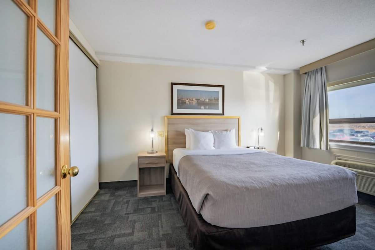 A hotel room with a bed, a nightstand, a framed picture on the wall, and a window with a view.