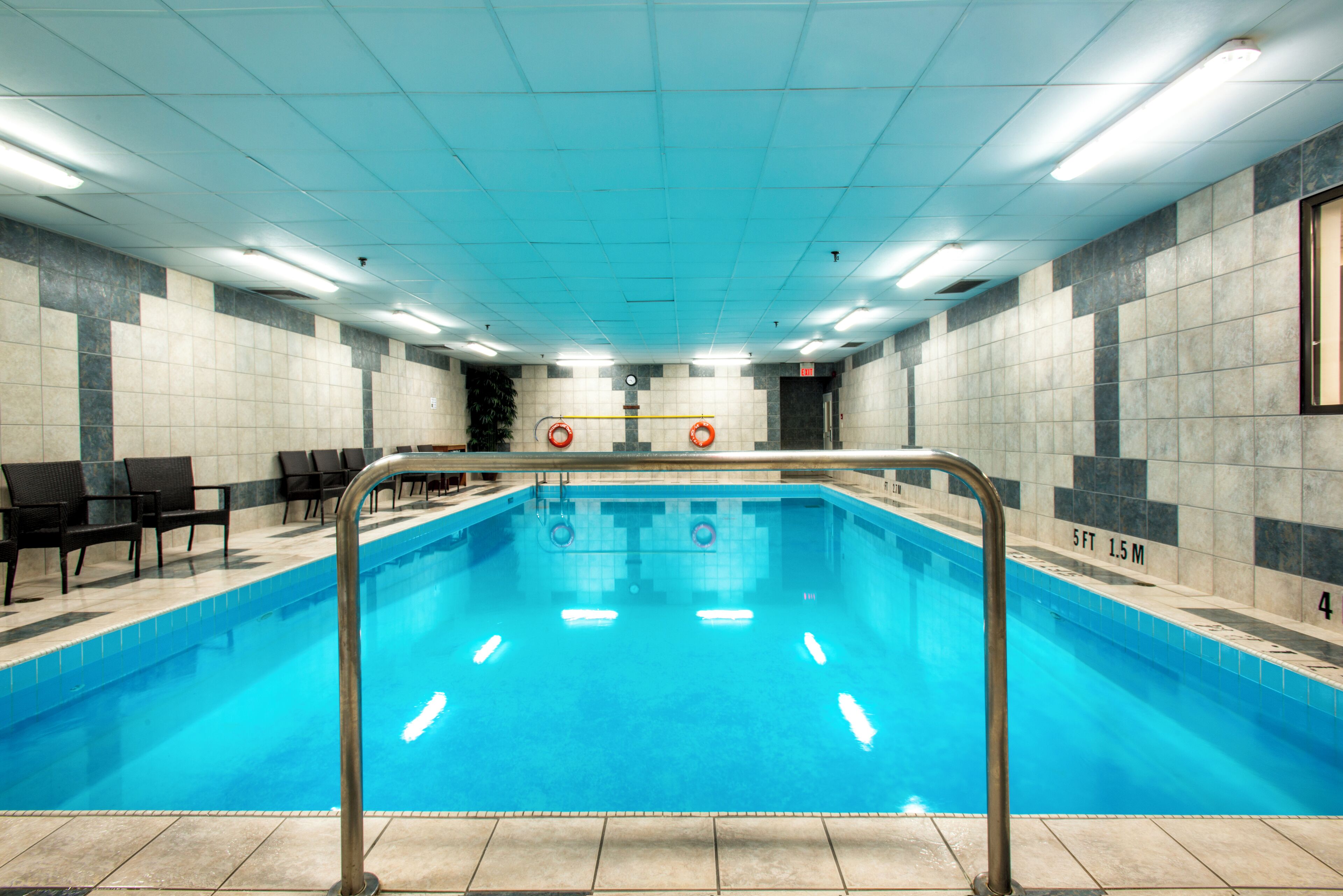 Una piscina con barandilla metálica, paredes con azulejos e iluminación fluorescente en el techo.