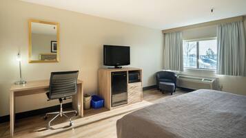 Habitación de hotel con cama, escritorio y silla, televisor, microondas, mueble pequeño y ventana con cortinas.