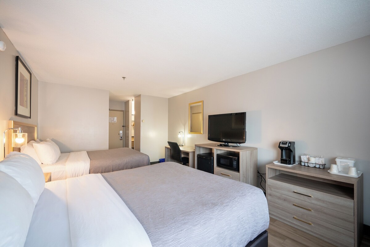 A hotel room with two beds, a desk with a computer, a television, a coffee maker, and a microwave.