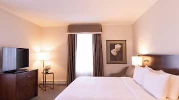 Un cuarto de hotel con una cama grande, un televisor en una cómoda de madera, una lámpara y un cuadro en la pared.