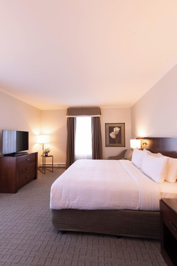 A hotel room with a large bed, a television on a wooden dresser, a lamp, and a framed picture on the wall.