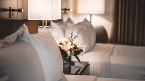 Habitació d'hotel amb un llit ben arropat, una taula de nit amb una làmpada i un ram de flors.