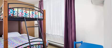 A bunk bed with a colorful quilt, a blue chair, and a window with purple curtains.