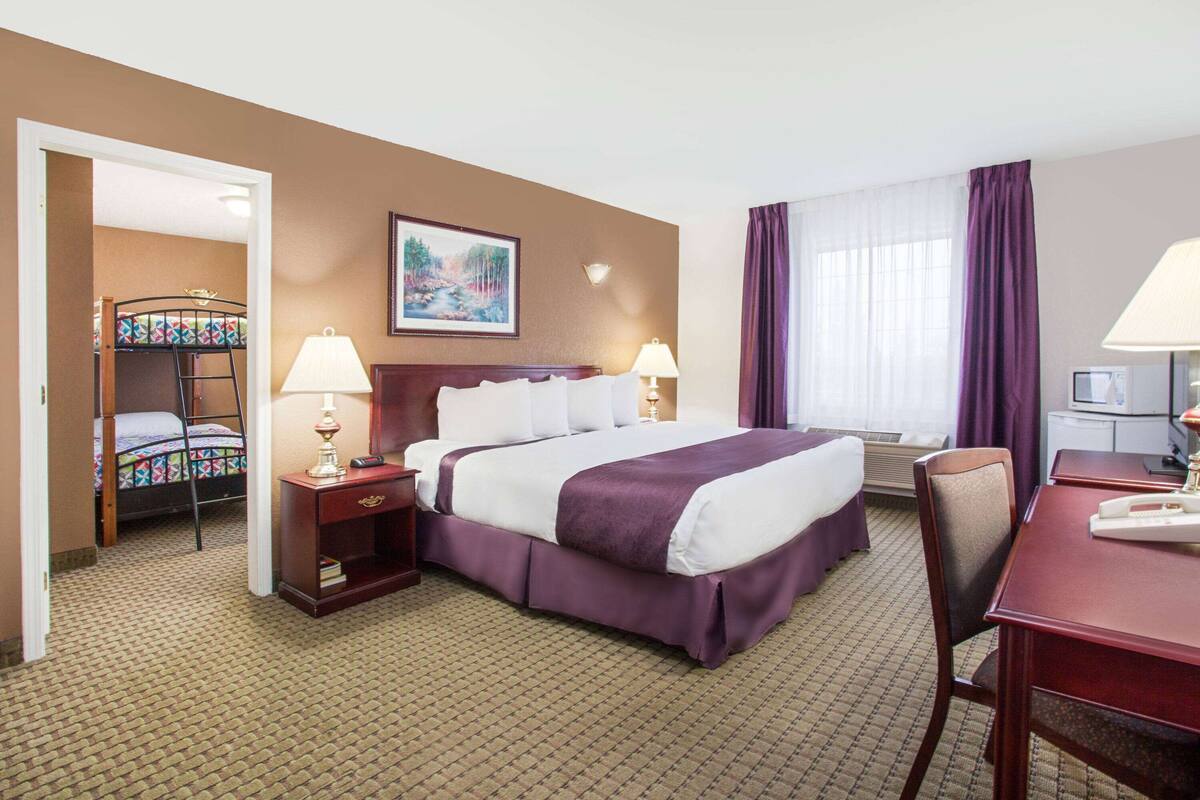 Une chambre d’hôtel comprenant un lit, deux tables de chevet avec des lampes, un bureau avec une chaise, une fenêtre avec des rideaux et un tableau au mur.