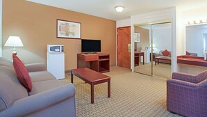 A hotel room with a sofa, a small table, a TV, a microwave, and a mirror. - Ramada by Wyndham Red Deer Hotel and Suites (Red Deer)