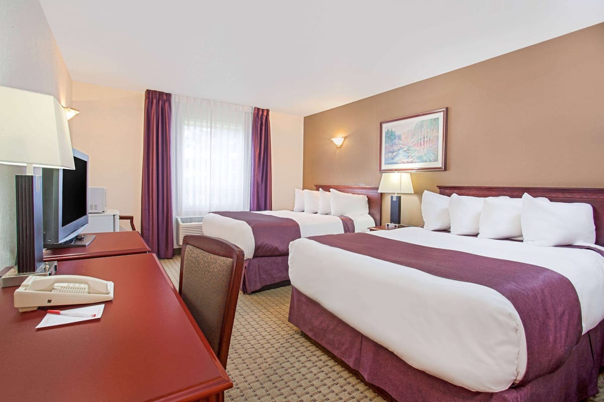 Une chambre d’hôtel avec deux lits, un bureau avec un téléphone, une télévision et une fenêtre avec des rideaux.