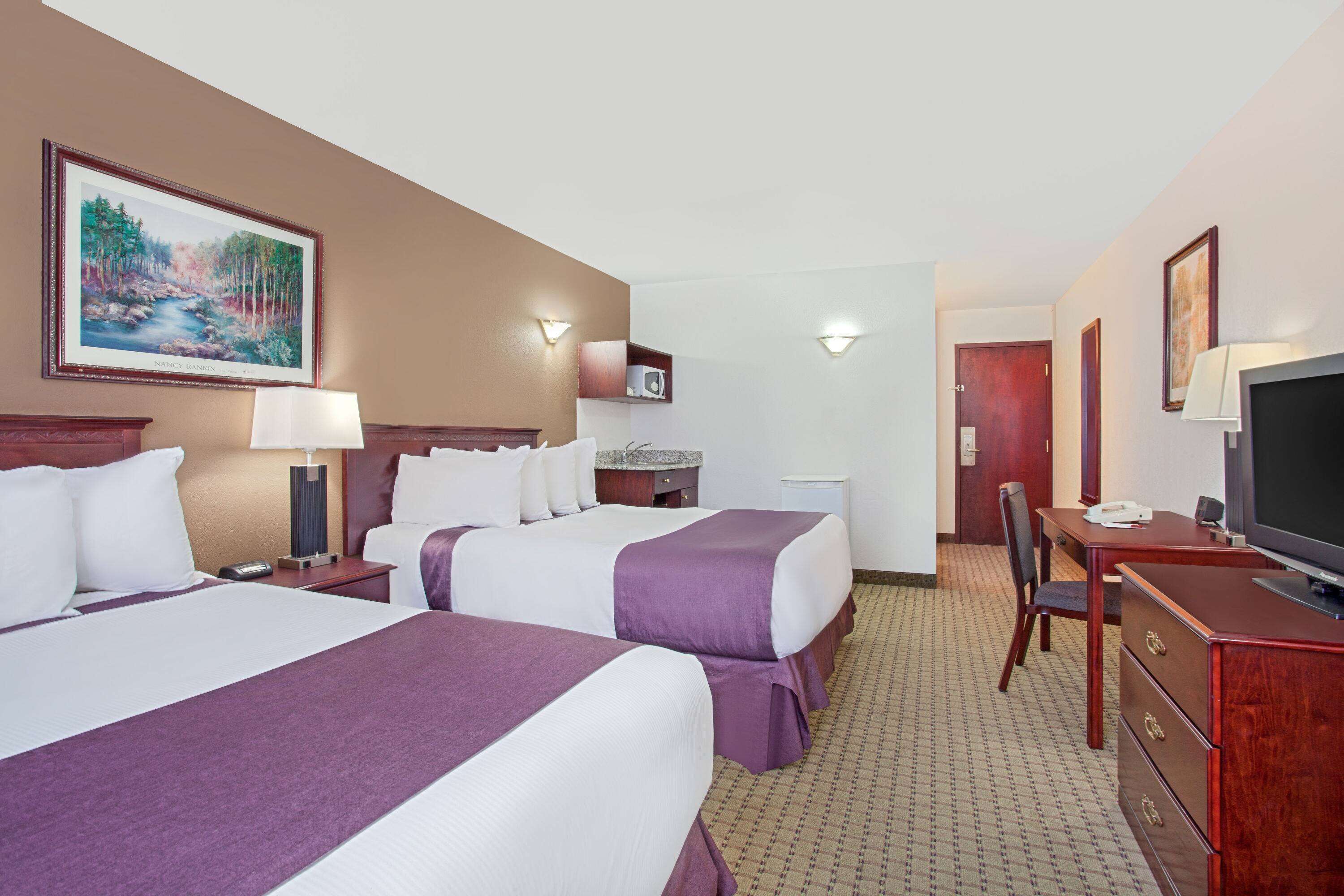 A hotel room with two beds, a desk, a chair, a television, and a painting on the wall.