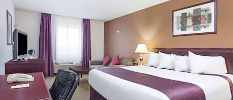 Hotellihuone, jossa on suuri sänky, kirjoituspöytä, jossa on puhelin, tuoli, televisio ja ikkuna, jossa on violetit verhot.