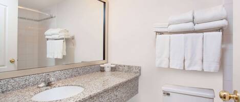 Un baño con lavamanos de encimera de granito, un espejo con iluminación, inodoro y toallas apiladas en un perchero.