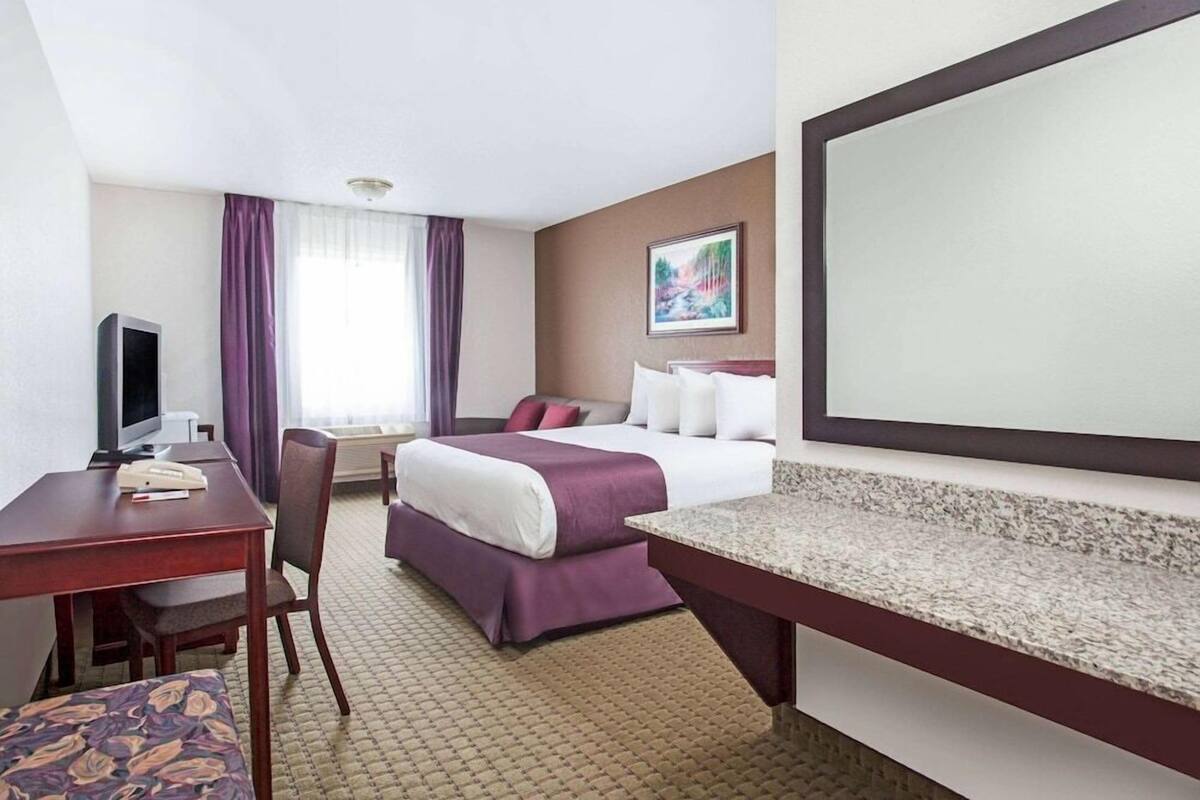 Une chambre d’hôtel comprenant un lit, un bureau avec une chaise, une télévision et un grand miroir.