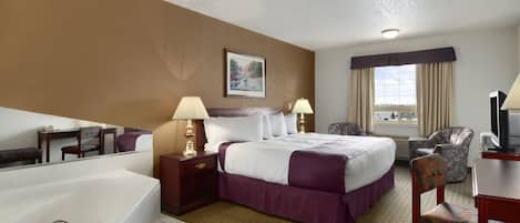Habitación de hotel con una cama grande, dos mesitas de noche con lámparas, una silla, un escritorio con computadora, un ventanal con cortinas y un baño con bañera y lavamanos.