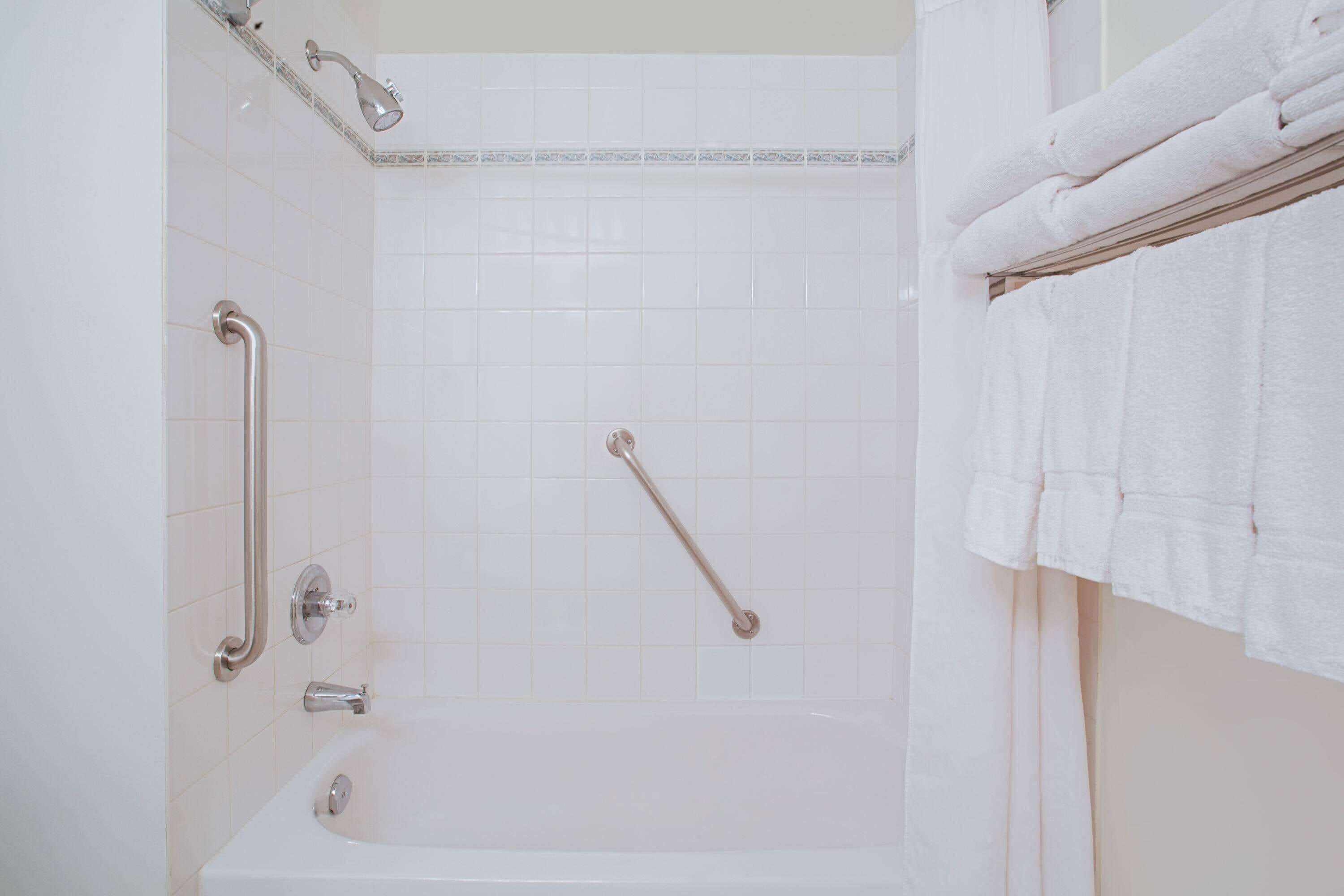 A bathroom with a white bathtub, grab bars, and a towel rack.