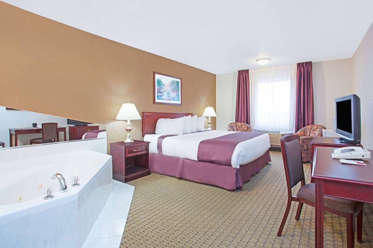 Une chambre d’hôtel avec un grand lit, un bureau avec une chaise, une télévision, une lampe de bureau, une table de chevet et une grande baignoire.