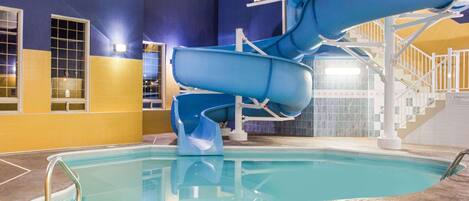 An indoor swimming pool with two blue water slides and a staircase leading to a higher level.