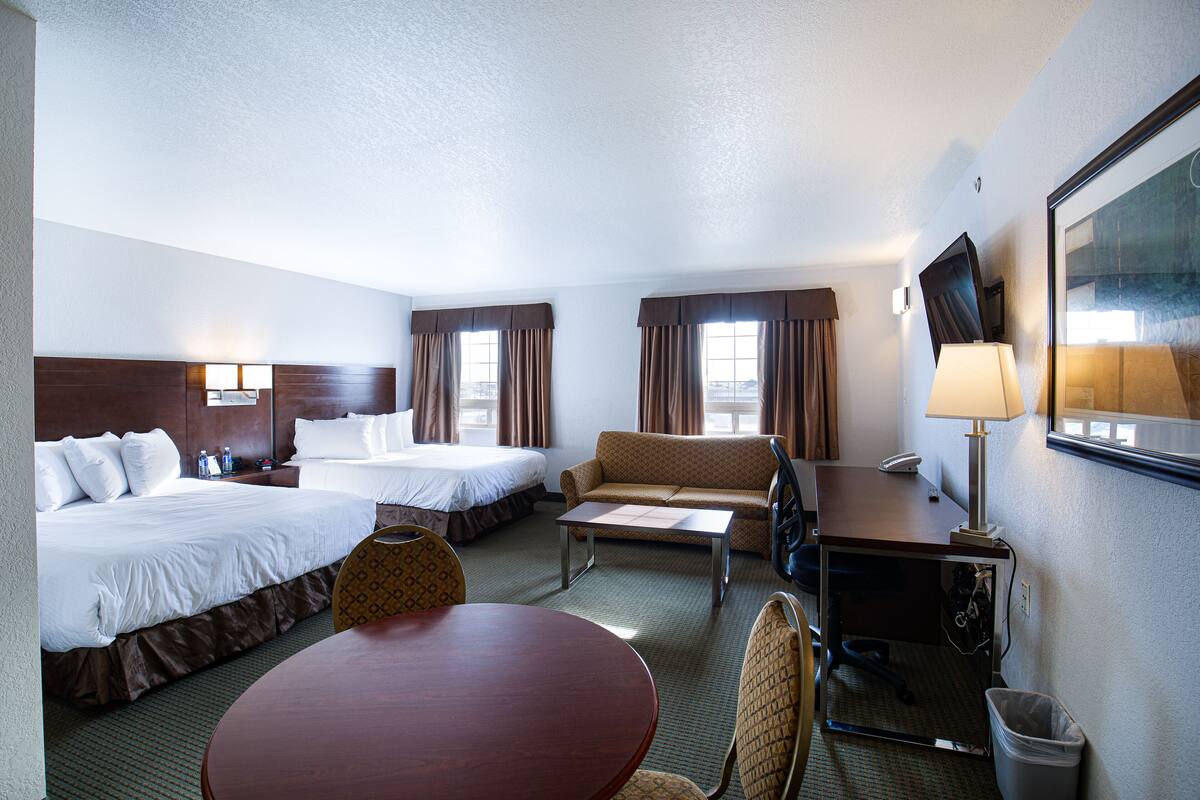 A hotel room with two beds, a sofa, a desk, a chair, a table, and a TV.