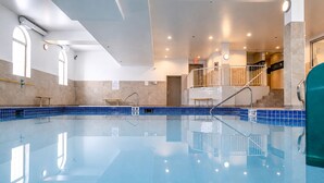 An indoor swimming pool with clear water, tiled walls, and a staircase leading to an upper level.