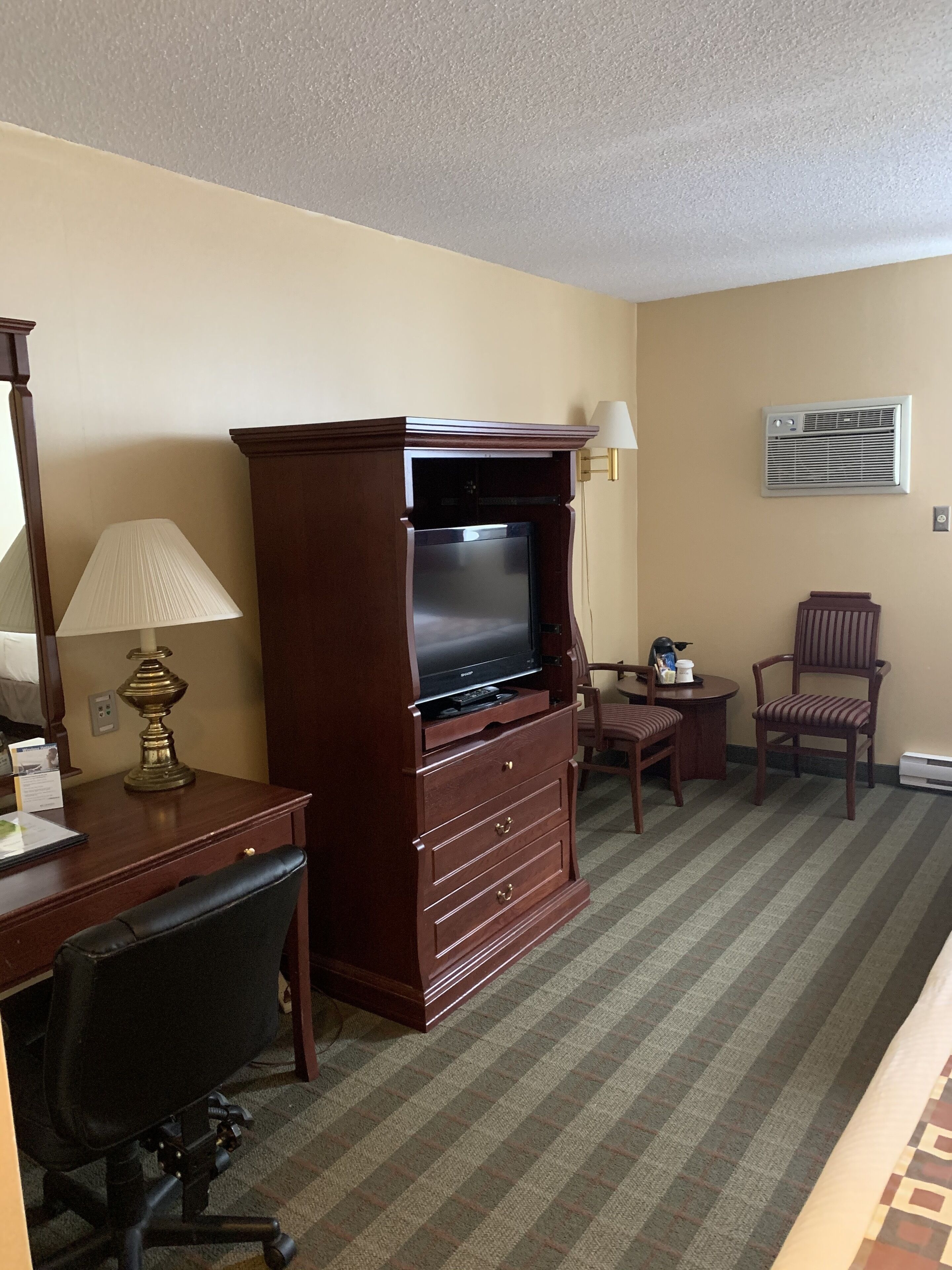 Habitación de hotel con un mueble de entretenimiento de madera, un escritorio con lámpara, una silla y una mesita.