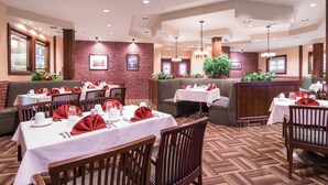 A restaurant with multiple tables set for dining, featuring a brick wall and wooden furniture. - Albatross Hotel (Gander)
