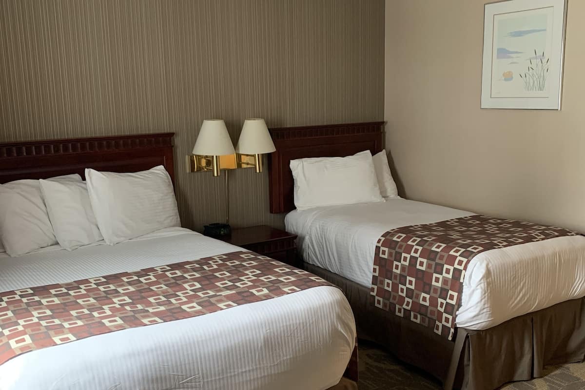 A hotel room with two beds, each with a patterned bedspread, a wooden headboard, and two bedside lamps.