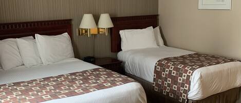 A hotel room with two beds, each with a patterned bedspread, a wooden headboard, and two bedside lamps.