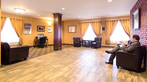 A hotel lobby with a reception desk, seating area, and a large window with curtains. - Albatross Hotel (Gander)
