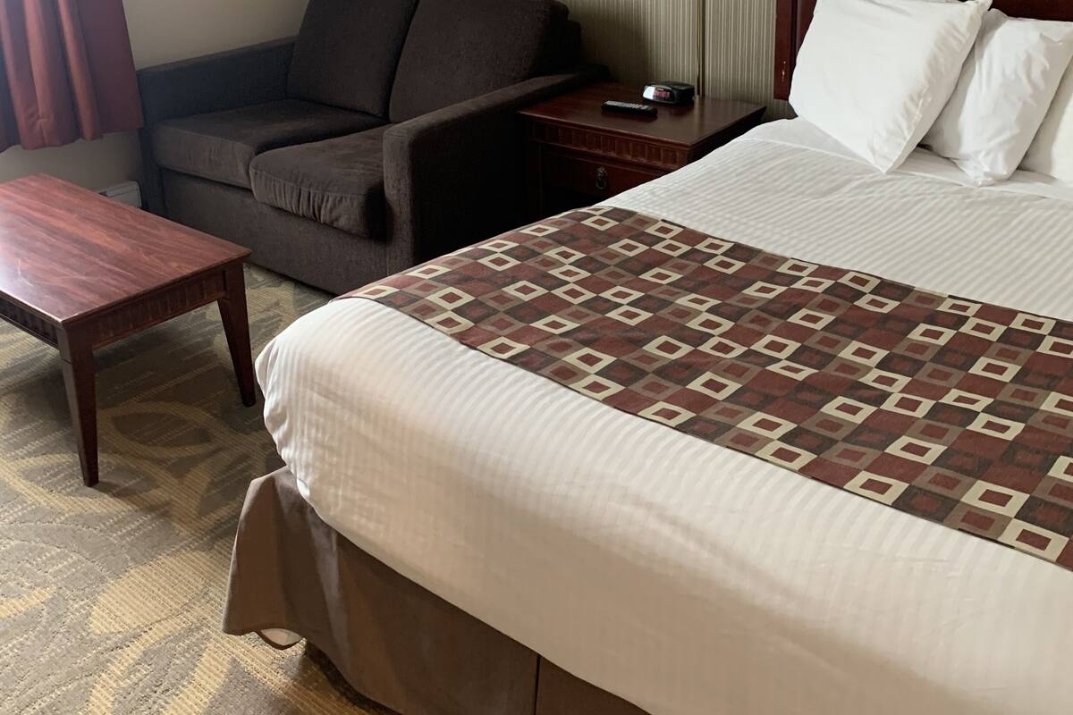 A hotel room with a bed, a desk, a chair, and a nightstand with lamps.