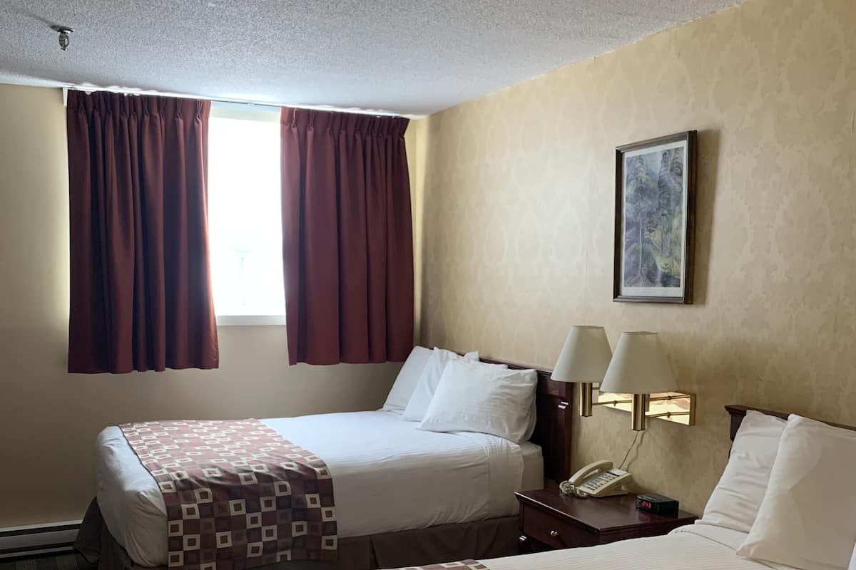 A hotel room with two beds, a nightstand with a lamp, a telephone, and a painting on the wall.