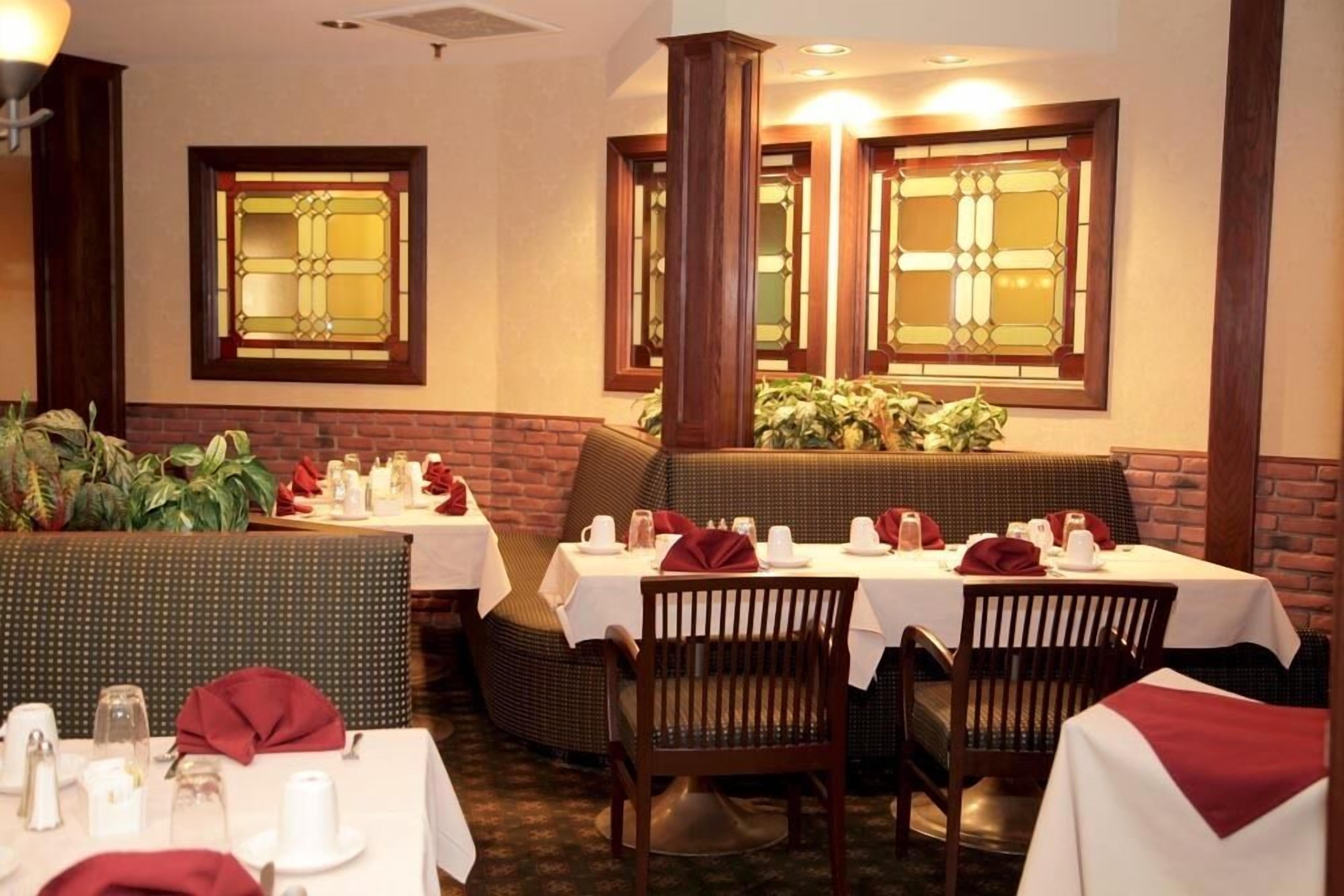 Un restaurant avec des banquettes et des tables, chacune agrémentée d’une nappe blanche et de serviettes rouges.