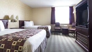 A hotel room with two beds, a desk, a chair, a TV, and a window with curtains. - Albatross Hotel (Gander)