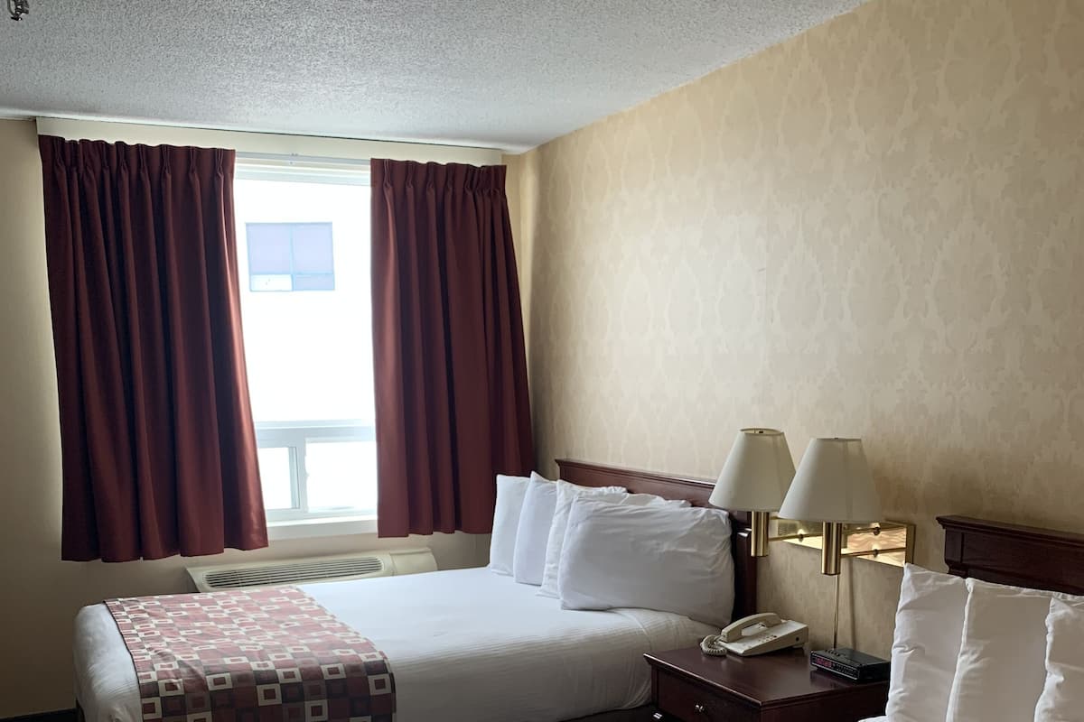 A hotel room with two beds, a window with curtains, a bedside table with lamps, and a phone.