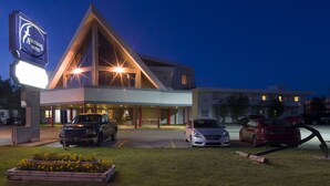 A hotel with a modern design, featuring a prominent triangular glass facade and a large illuminated sign. - Albatross Hotel (Gander)