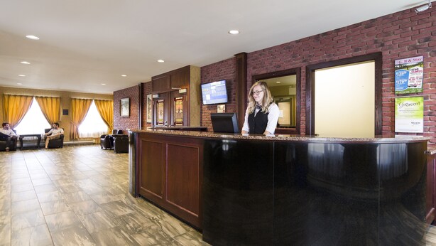 A reception area with a black counter, a TV, and a brick wall. - Albatross Hotel (Gander)