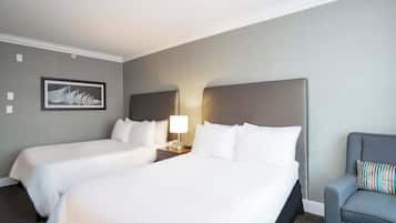 Una habitació d'hotel amb dos llits, un armari gris, una taula de nit amb una làmpada i un quadre encarregat a la paret.