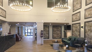 Un hall d’entrée spacieux avec un comptoir de réception, deux lustres, un canapé vert et une table basse.