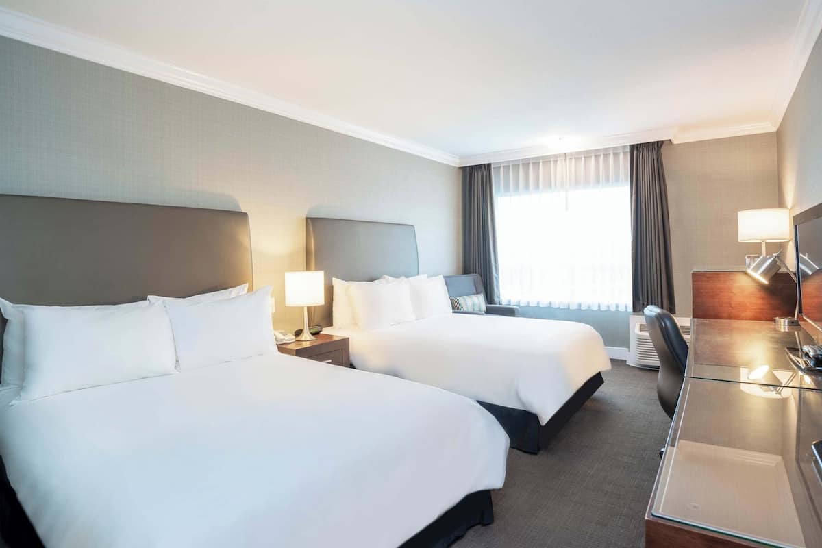 A hotel room with two beds, a desk, and a chair.