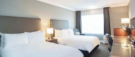A hotel room with two beds, a desk, and a chair.