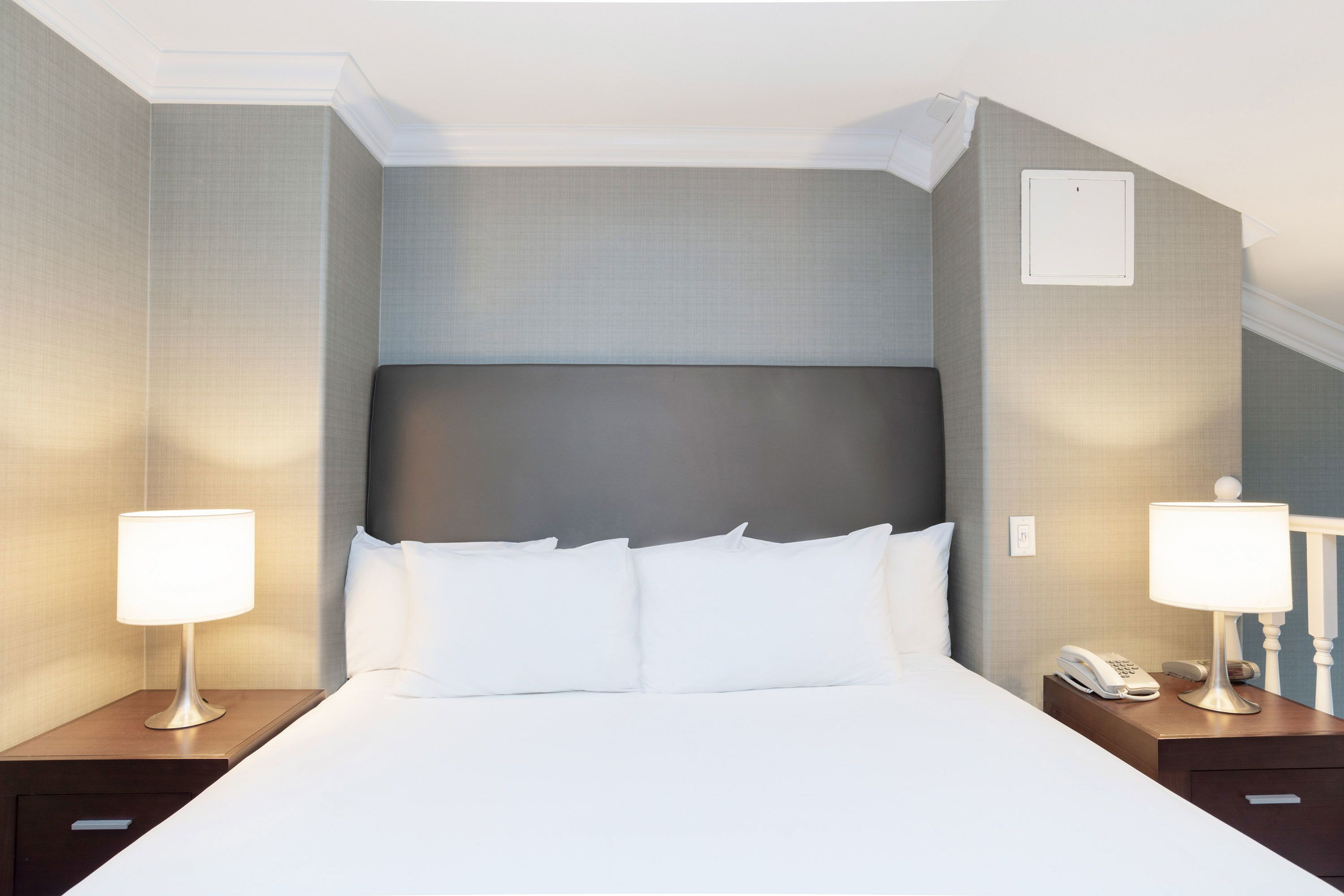 Een hotelkamer met een groot bed, twee nachtkastjes, een telefoon en een lichtschakelaar aan de muur.