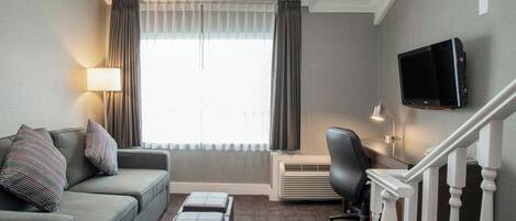 Habitación de hotel con sofá, televisor de pantalla plana en la pared, escritorio con silla y una escalera.