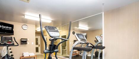 A hotel gym with exercise equipment, a clock, and a mirror reflecting the room.
