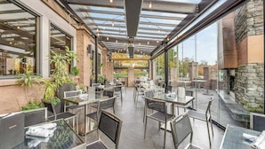 Un espace extérieur aménagé pour les repas, avec des tables et des chaises en verre, entouré de murs en pierre et agrémenté de plantes en pot.