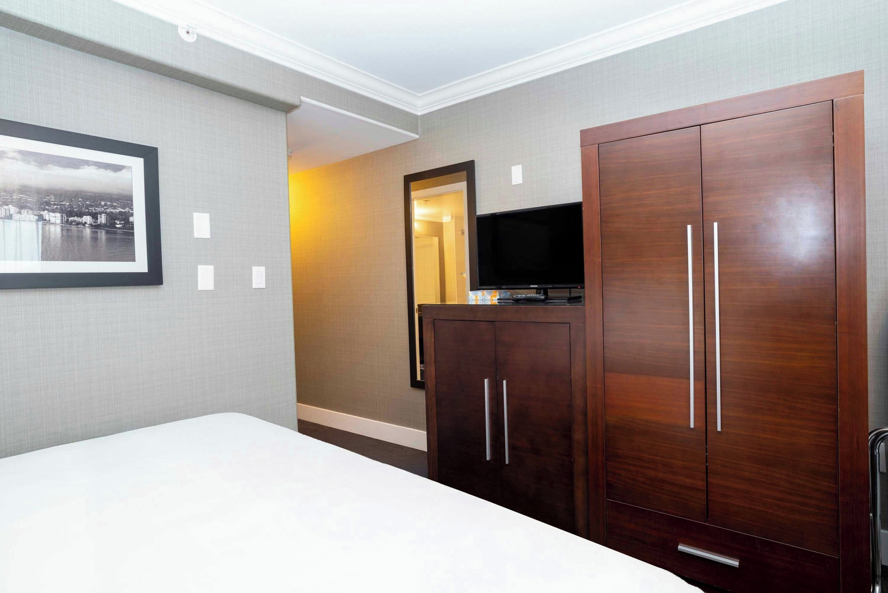 Quarto de hotel com uma cama, um guarda-roupa, uma televisão e um quadro na parede.