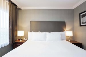 Habitación de hotel con una cama grande, dos mesitas de noche con lámparas, un teléfono y un cuadro en la pared.