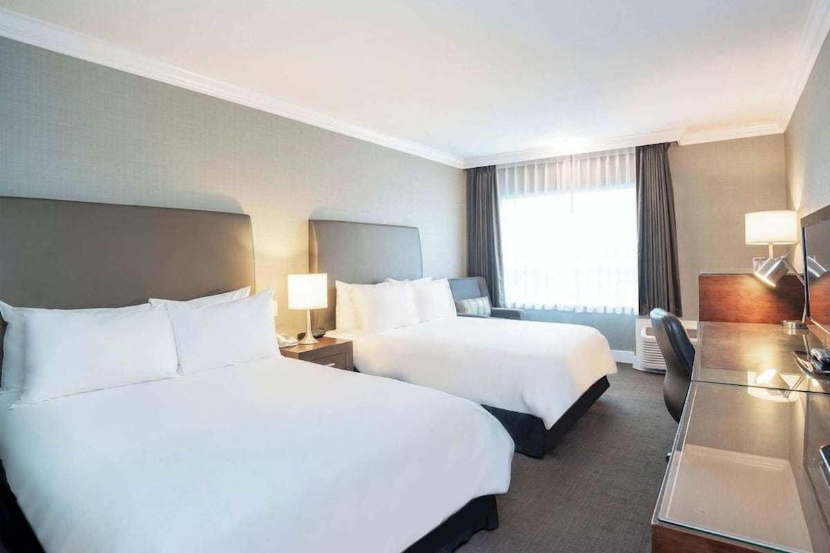 A hotel room with two beds, a desk, and a chair.